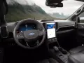 Wnętrze nowoczesnego Ford SUV z dużym ekranem dotykowym i cyfrowymi zegarami. Widok na górzysty krajobraz przez przednią szybę.