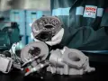 Mechanik w białych rękawiczkach prezentuje części turbosprężarki, sugerując domowe ustawienie sztangi turbiny.