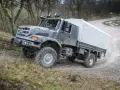 Szary Mercedes Zetros z plandeką pokonuje trudny teren leśnej drogi.
