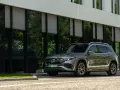 Nowy Mercedes 4x4, elegancki SUV, zaparkowany przed nowoczesnym budynkiem z zielonymi odbiciami drzew w szybach.