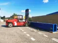 Czerwony wózek widłowy przygotowuje się do przeładunku długiego, niebieskiego elementu. To przykład sprawnego cross dockingu.
