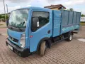 Niebieska ciężarówka Renault Maxity z otwartą skrzynią ładunkową, zaparkowana na brukowanym podjeździe.