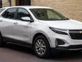 Biały Chevrolet Equinox stoi zaparkowany na brukowanej ulicy, obok ceglanego budynku.