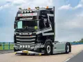 Czarna Scania V8 z szarymi pasami, z napisem "TERMOTRAFIK" i licznymi światłami, gotowa do trasy.