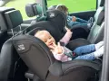 Uśmiechnięte niemowlę w foteliku Britax Römer, obok starsze dziecko. Od kiedy dziecko może jeździć z przodu? To pytanie nurtuje wielu rodziców.