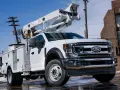 Biały Ford F-750 z podnośnikiem koszowym gotowy do pracy przy liniach energetycznych.