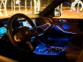 Wnętrze luksusowego BMW x5 nocą, oświetlone niebieskim ambientowym światłem. Za oknem świąteczne iluminacje.