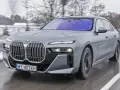 Szary BMW Serii 7 w ruchu, z widocznym grillem i reflektorami. Sprawdź aktualną bmw 7 cena.