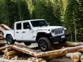 Biały jeep pickup Rubicon pokonuje przeszkodę z bali drewna w lesie.