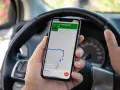 Ręce kierowcy trzymają telefon z nawigacją. Używanie telefonu podczas jazdy grozi mandatem.
