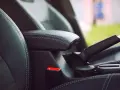 Wnętrze samochodu: czarna skórzana tapicerka, podłokietnik, hamulec ręczny i przycisk auto hold.