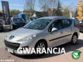 Srebrny Peugeot 207 1.4 benzyna na placu samochodowym, z napisem "GWARANCJA".