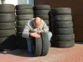 Mężczyzna sprawdza stan wyząbkowanych opon, które leżą obok stosów innych opon.