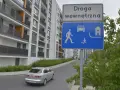 Droga wewnętrzna w terenie zabudowanym. Znak informuje o ruchu pieszych, samochodów i domów.