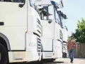Kierowca idzie obok rzędu białych ciężarówek. To właśnie spedycja co to – transport towarów na dużą skalę.