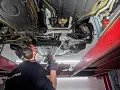 Pracownik w masce i słuchawkach wykonuje czyszczenie suchym lodem podwozia samochodu na podnośniku.