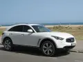 Białe infiniti auto zaparkowane przy plaży, z widokiem na morze i ludzi odpoczywających na piasku.