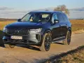 Ciemnoszary Volvo XC90 na polnej drodze, z widokiem na pola i drzewa w tle.