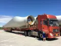 Pomarańczowy tir przewozi gigantyczne łopaty turbin wiatrowych. Kierowca przygotowuje się do dalszej podróży.