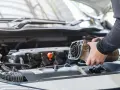 Mechanik wymienia rozrusznik w aucie. Widoczny jest silnik i ręce trzymające zużyty element.