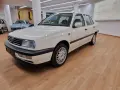 Biały Volkswagen Vento z lat 90. stoi na drewnianej podłodze w salonie samochodowym.