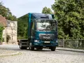 Nowy MAN TGM w kolorze głębokiego turkusu jedzie brukowaną uliczką, mijając stare kamienice i bujną zieleń.