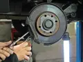 Dłonie mechanika z narzędziami przy hamulcu tarczowym samochodu.