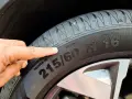 Palec wskazuje na oponę, gdzie widoczny jest rozmiar 215/60 R16. To ważny element, który określa indeks prędkości opon.