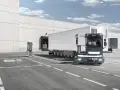 Ciężarówka Terberg z naczepą stoi przy ładowarce elektrycznej przed magazynem.