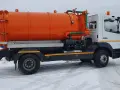 Pomarańczowy pojazd asenizacyjny z beczką i zielonymi wężami stoi na zaśnieżonej drodze.
