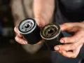 Nowy i zużyty filtr oleju w dłoniach mechanika. Wymiana filtra oleju to kluczowy element dbania o silnik.