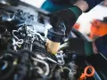 Mechanik w czarnych rękawiczkach dokonuje wymiany filtra paliwa w silniku samochodu.