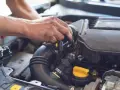 Ręce mechanika pracują przy silniku samochodu. Widoczny jest czarny przewód dolotowy i żółta zakrętka. p0101.