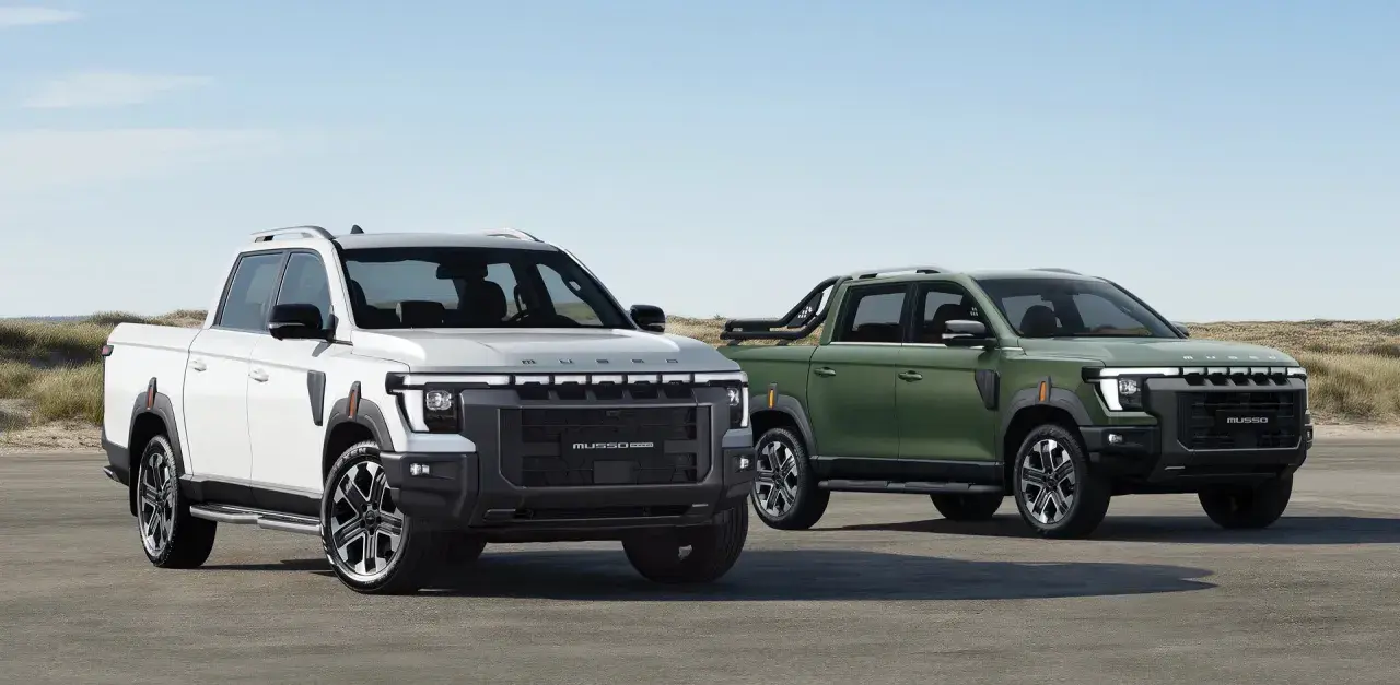 Dwa SsangYong pickup: biały i zielony, stojące na tle plaży i wydm.