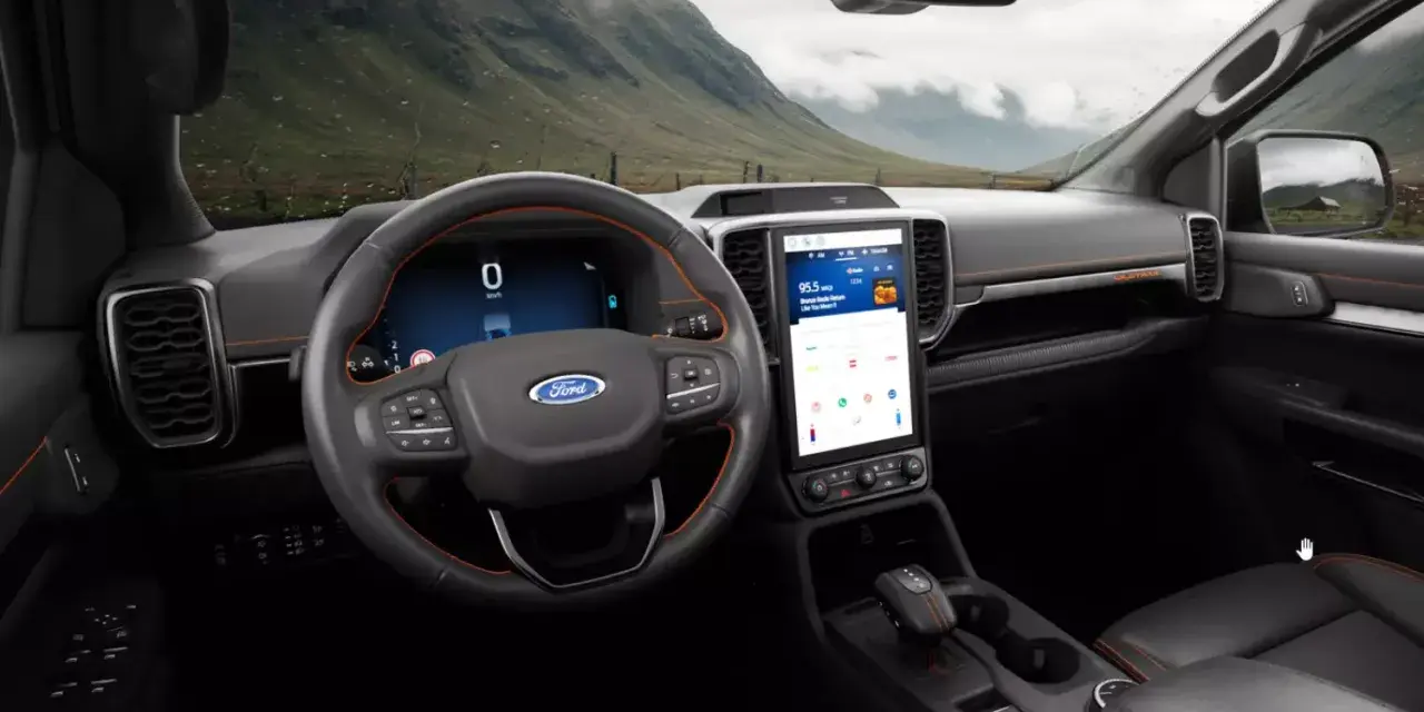 Wnętrze nowoczesnego Ford SUV z dużym ekranem dotykowym i cyfrowymi zegarami. Widok na górzysty krajobraz przez przednią szybę.