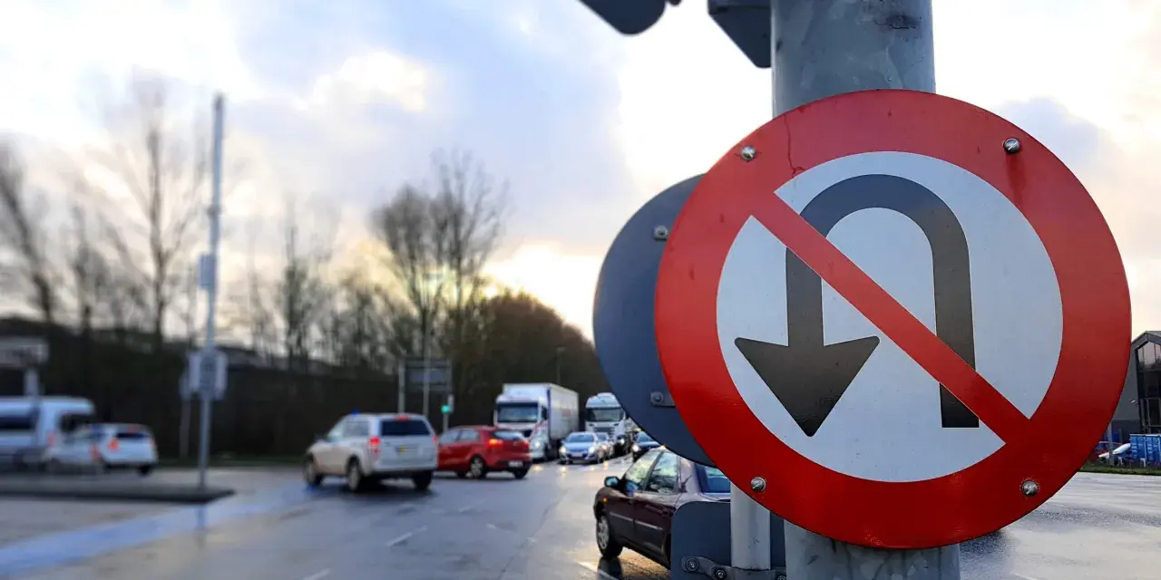 Znak zakazu zawracania na skrzyżowaniu. Samochody stoją w deszczu, czekając na zielone światło.
