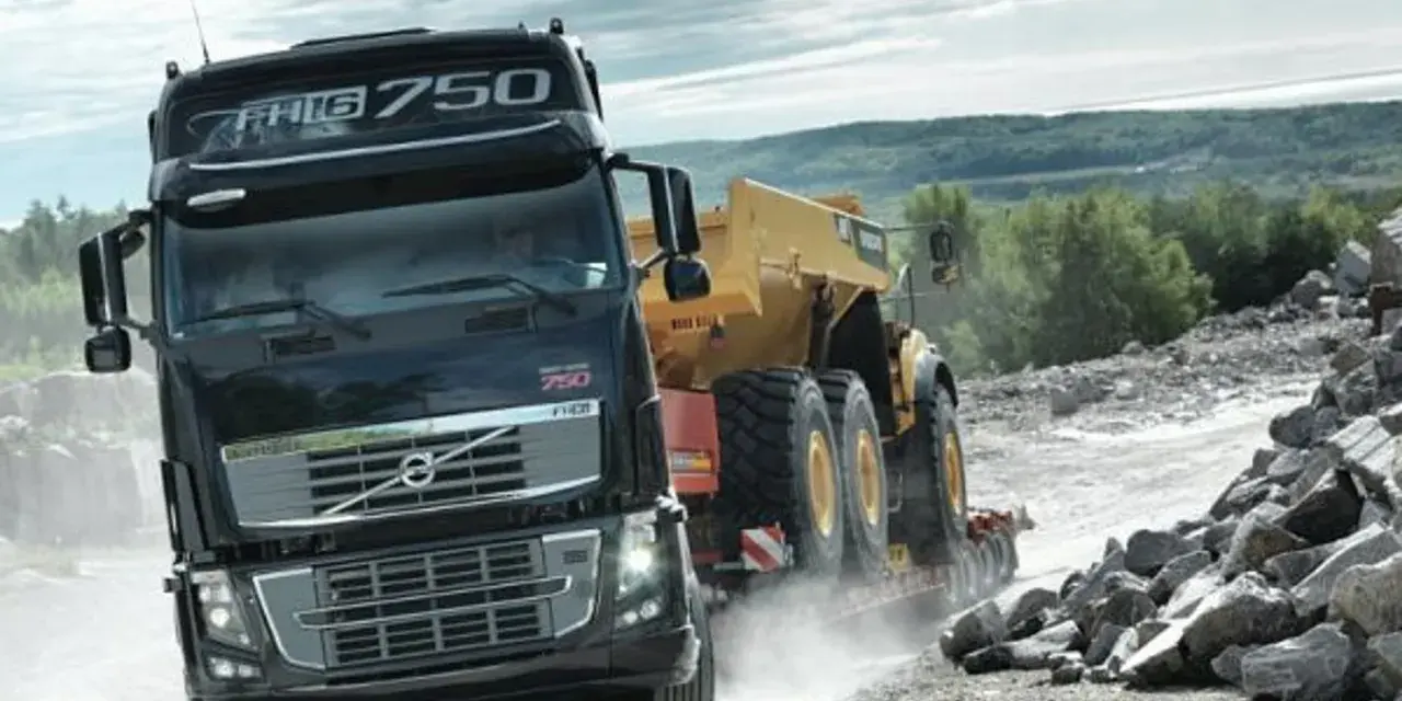 Ciężarówka Volvo FH16 750 z naczepą przewozi żółty wozidło przegubowe przez kamieniołom.