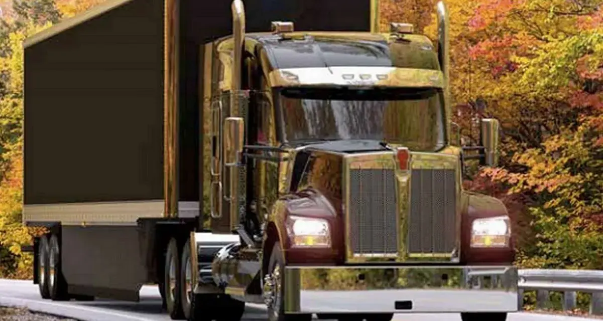 Błyszczący Kenworth W900 z przyczepą jedzie drogą wśród jesiennych drzew.