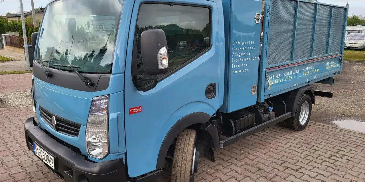 Niebieska ciężarówka Renault Maxity z otwartą skrzynią ładunkową, zaparkowana na brukowanym podjeździe.