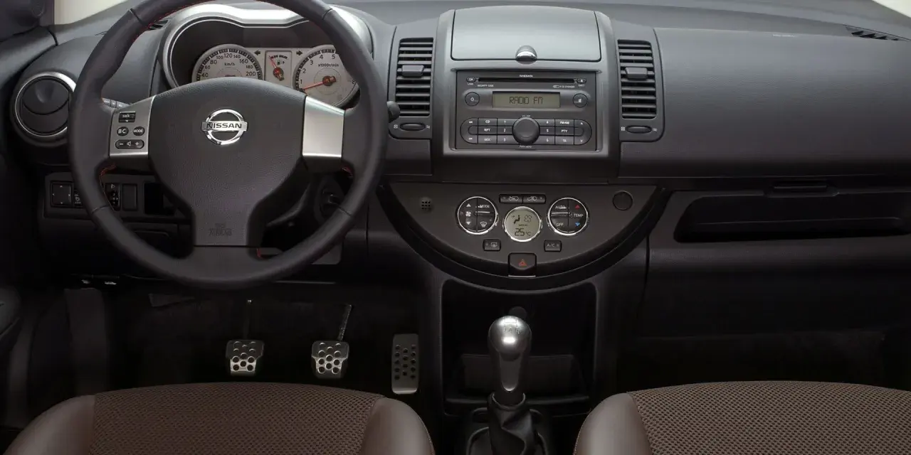Wnętrze Nissan Note E11: kierownica, deska rozdzielcza z radiem i zegarami, dźwignia zmiany biegów, fotele.