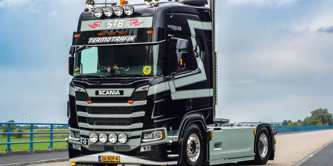 Czarna Scania V8 z szarymi pasami, z napisem "TERMOTRAFIK" i licznymi światłami, gotowa do trasy.