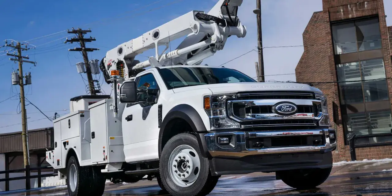 Biały Ford F-750 z podnośnikiem koszowym gotowy do pracy przy liniach energetycznych.