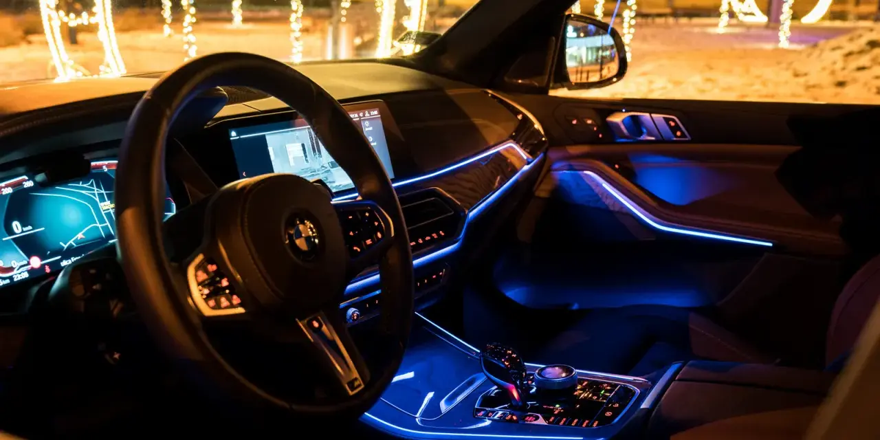 Wnętrze luksusowego BMW x5 nocą, oświetlone niebieskim ambientowym światłem. Za oknem świąteczne iluminacje.