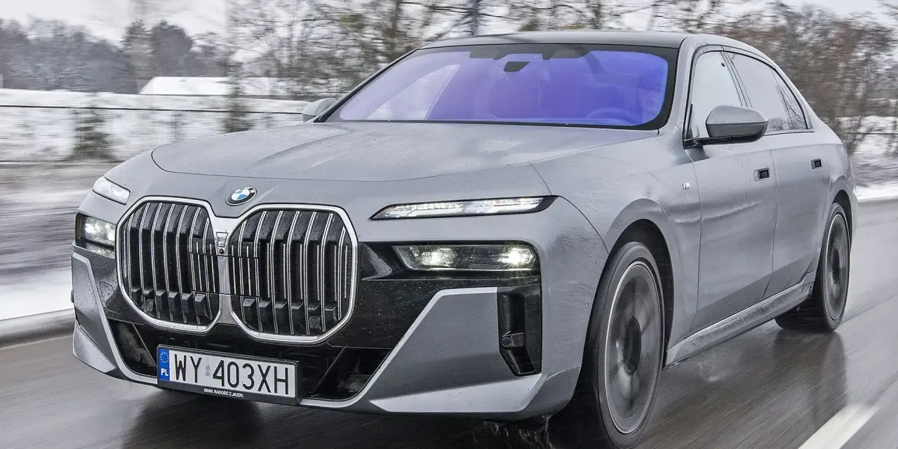 Szary BMW Serii 7 w ruchu, z widocznym grillem i reflektorami. Sprawdź aktualną bmw 7 cena.