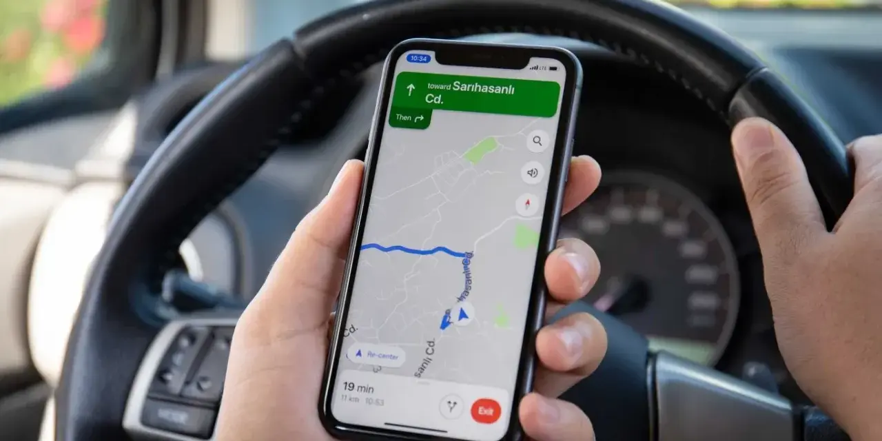 Ręce kierowcy trzymają telefon z nawigacją. Używanie telefonu podczas jazdy grozi mandatem.