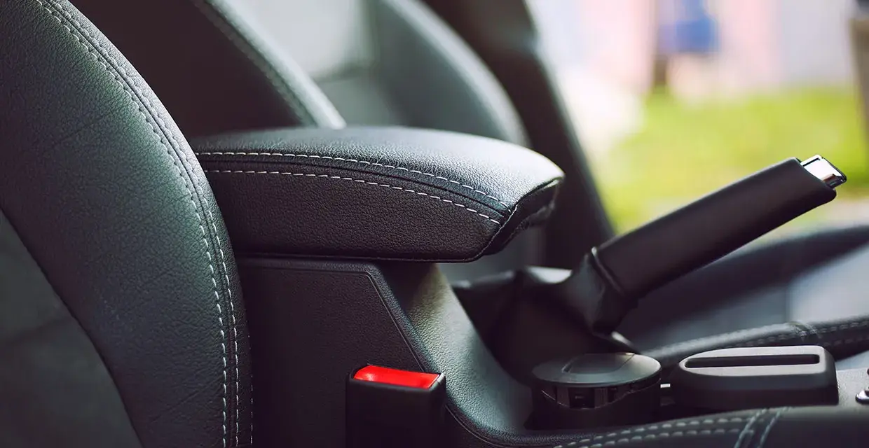 Wnętrze samochodu: czarna skórzana tapicerka, podłokietnik, hamulec ręczny i przycisk auto hold.