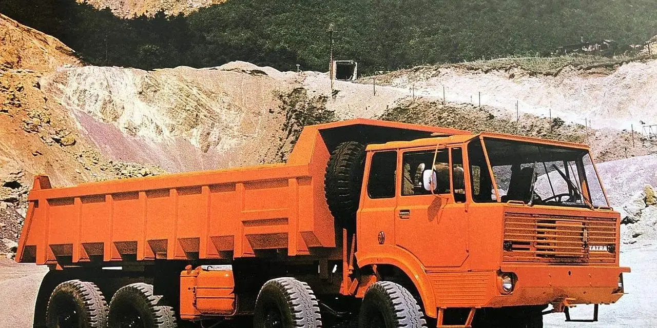 Pomarańczowy wywrotka Tatra 813 z zapasowym kołem na pace, gotowa do pracy w kamieniołomie.