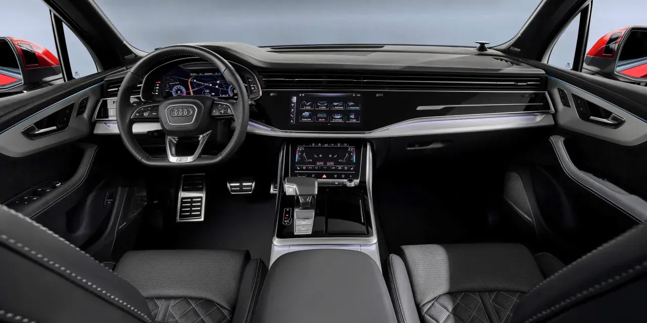 Wnętrze Audi Q7 z ekranami, kierownicą i skórzanymi fotelami.