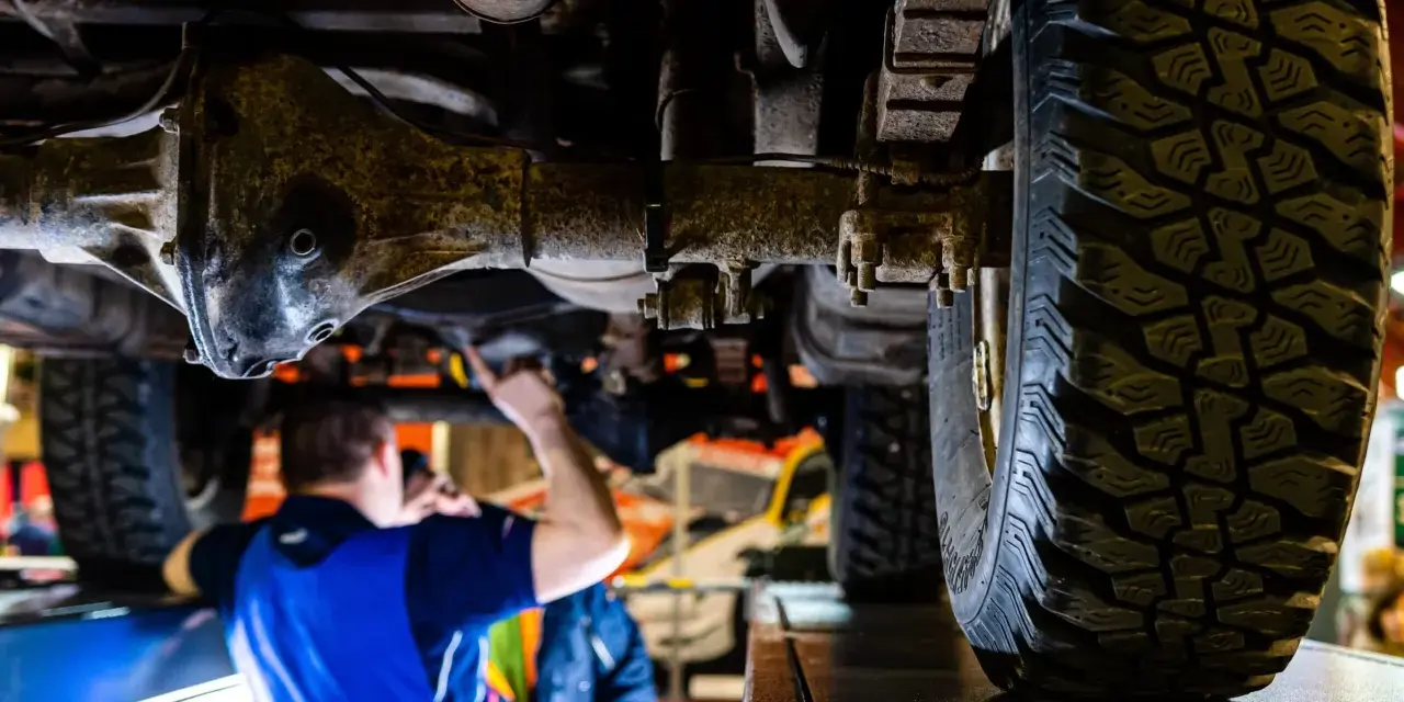 Mechanik bada podwozie terenowego Forda 4x4. Widoczna masywna oś i bieżnik opony.