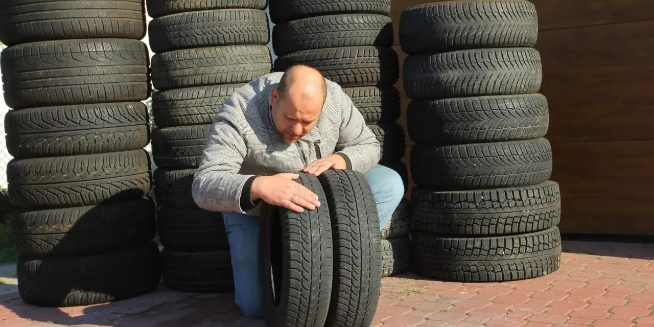 Mężczyzna sprawdza stan wyząbkowanych opon, które leżą obok stosów innych opon.